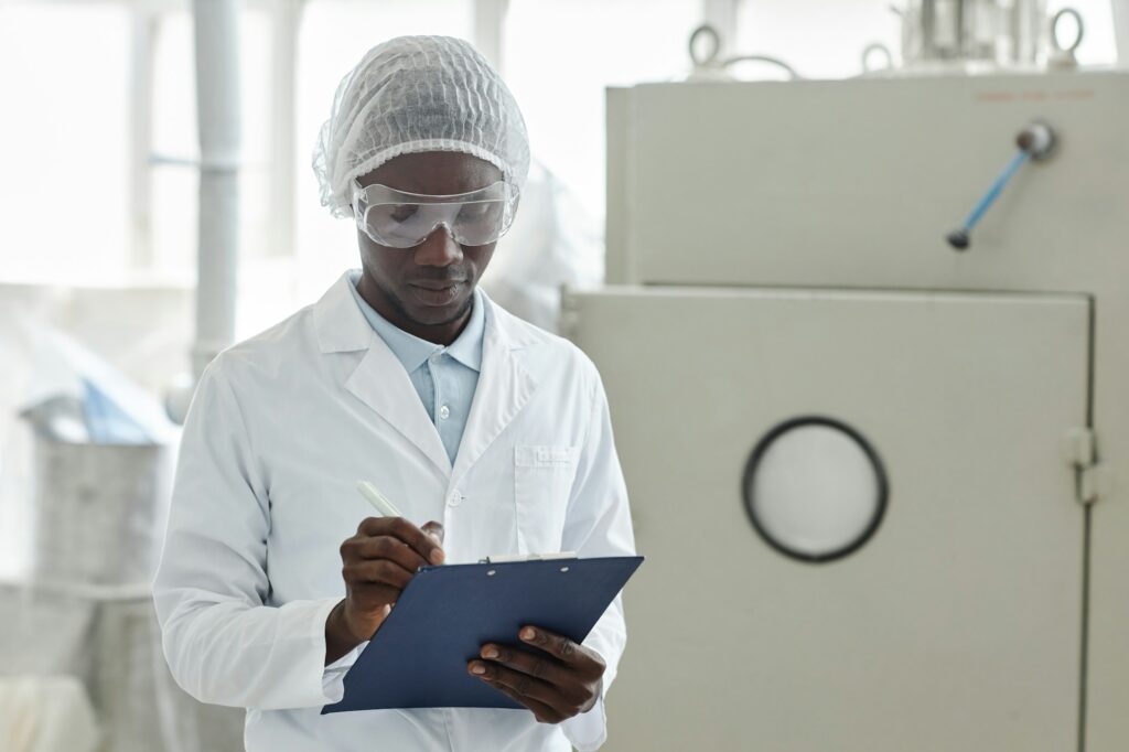 Black young man wearing lab coat in pharmaceutical factory