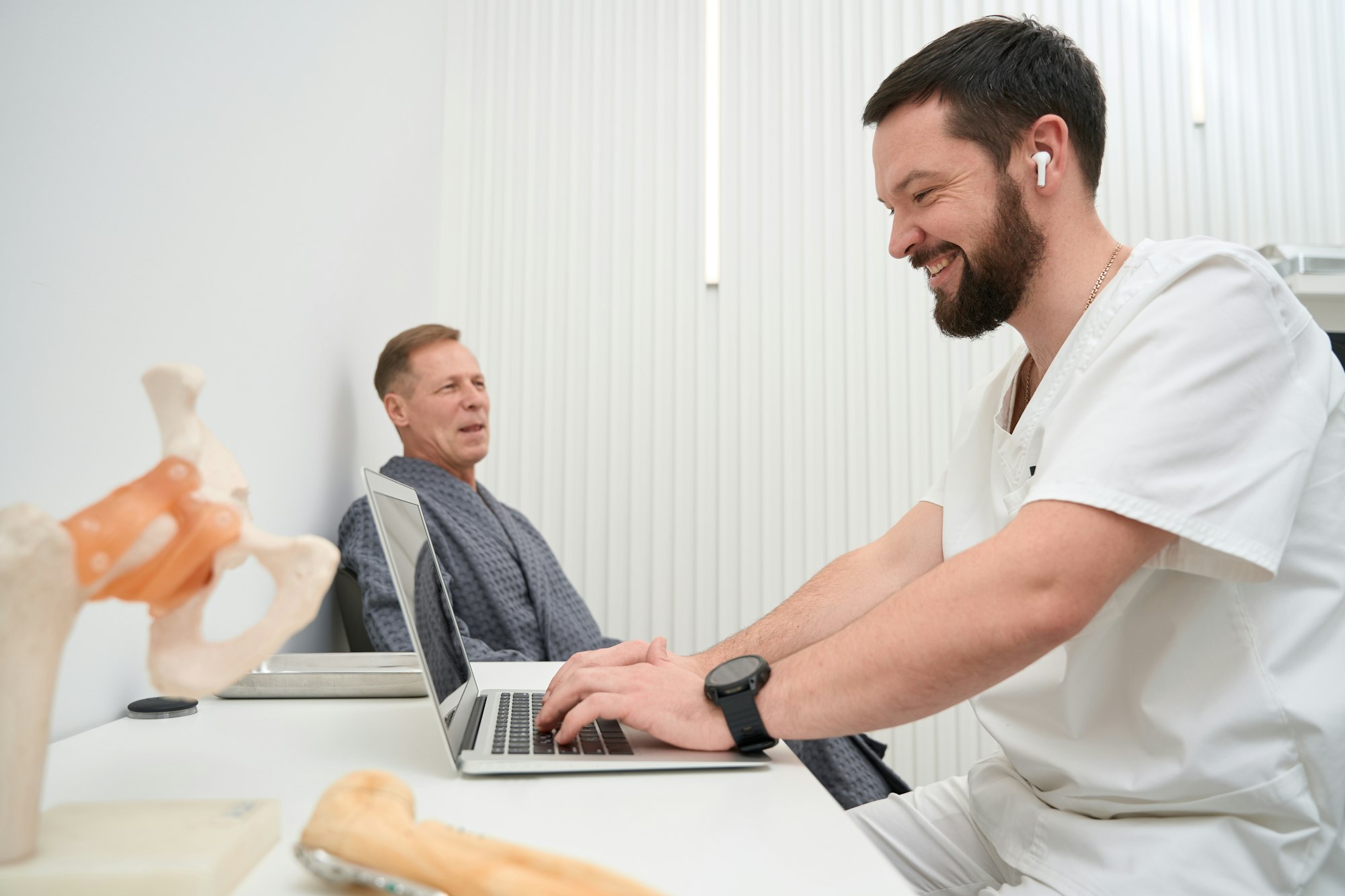 Cheerful medic putting data into his computer while consulting patient