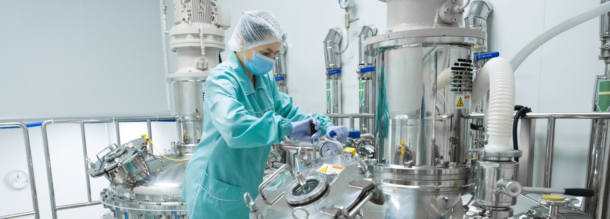 Pharmaceutical factory woman worker in protective clothing operating production line in sterile