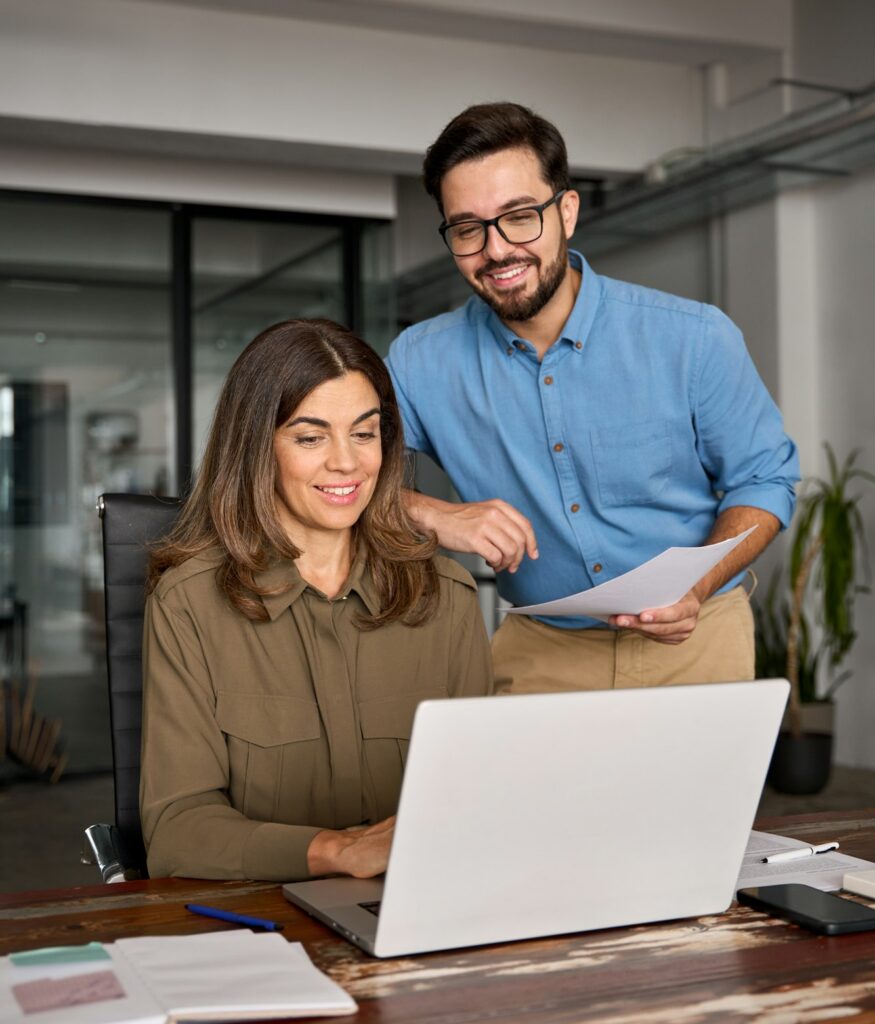 Happy young male manager helping mature woman employee explaining computer work.