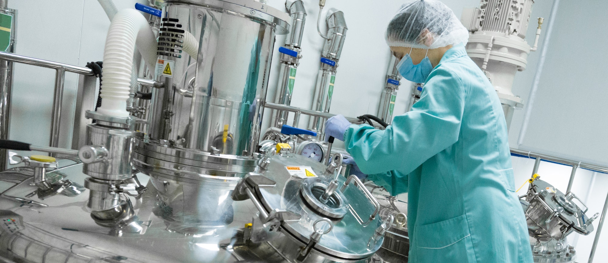 Pharmaceutical factory woman worker in protective clothing operating production line in sterile