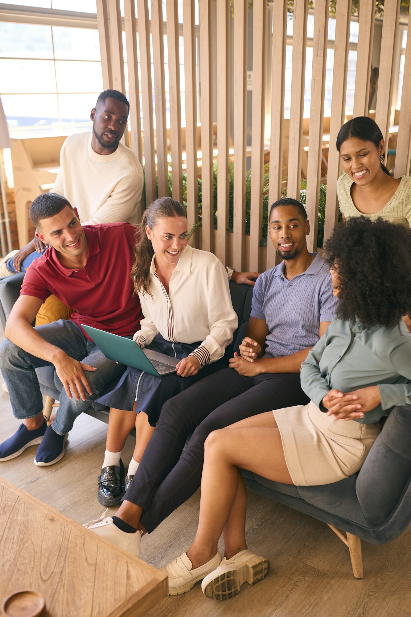 Multi-Cultural Business Team Sitting On Couch In Modern Open Plan Office Working On Laptop Together