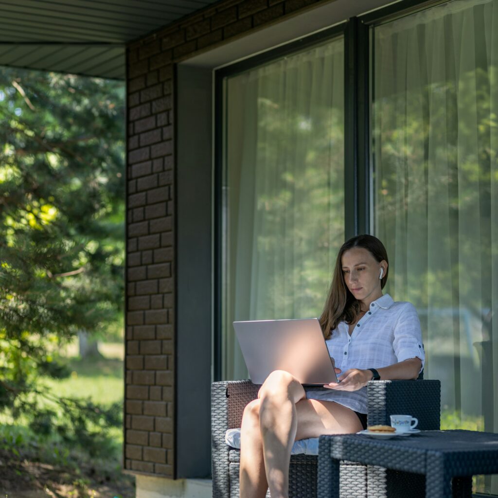 Young freelance woman using laptop sitting at the terrace in shade