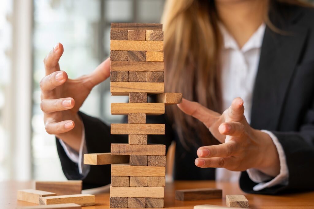 businesswoman holds her hand on a wooden block with a weak base. It is like a business risk mitigati