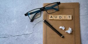 Process Auditing. Audit word written in wooden letters on a notepad, glasses, and a pen.