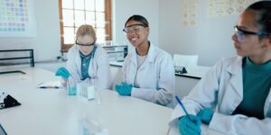 Science, students and learning in academy with test tubes, PPE and happy for higher education. Chem